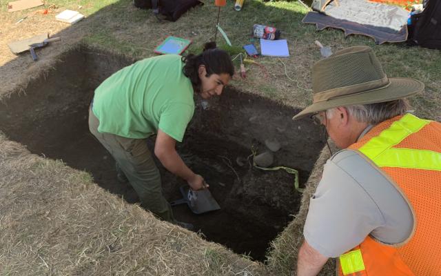 Student in archaeological dig with instructor looking on