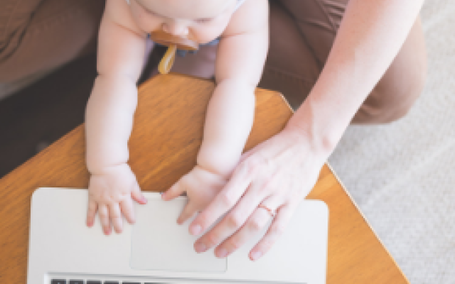 A mother with her infant in her lap as she works on a laptop