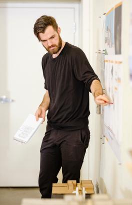 Master of Architecture student points to 2-dimensional work on wall