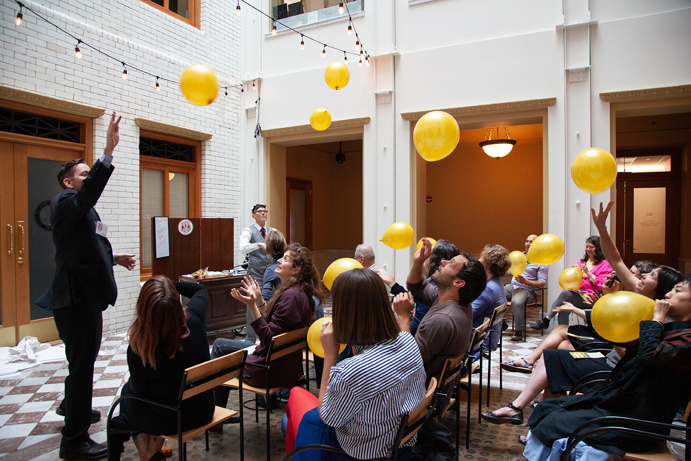 An audience at a social practice event play with yellow balloons