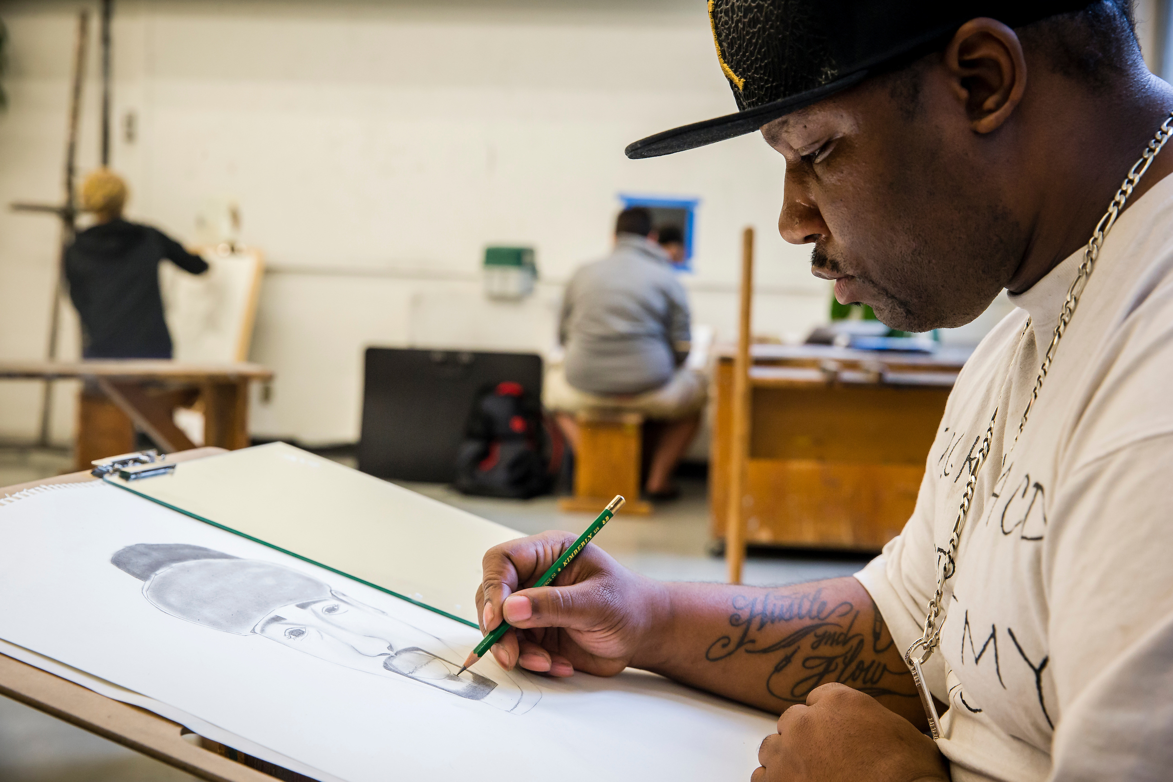 Student sketching in an art studio while seated at a drawing horse.