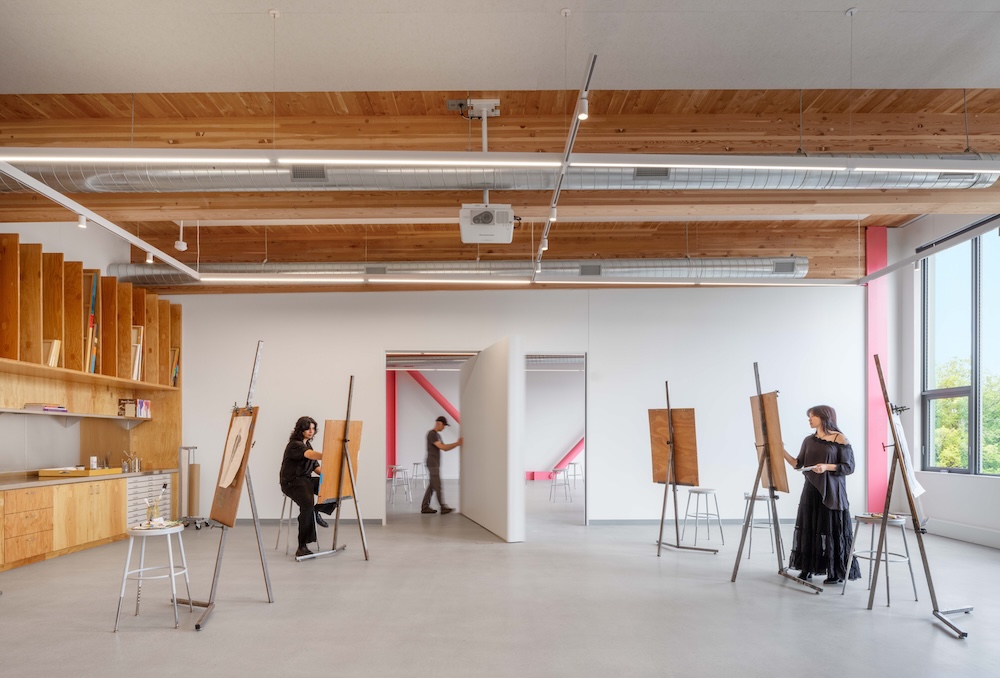 Students at easels in the drawing studio. A student opens a pivoting wall which gives a view into the painting studio beyond.