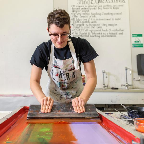 Student drawing colorful ink across a silk screen with a squeegee