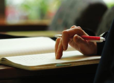 hand resting on a note pad holding a red pen, ready to take notes