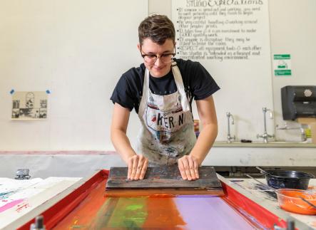 Student drawing colorful ink across a silk screen with a squeegee
