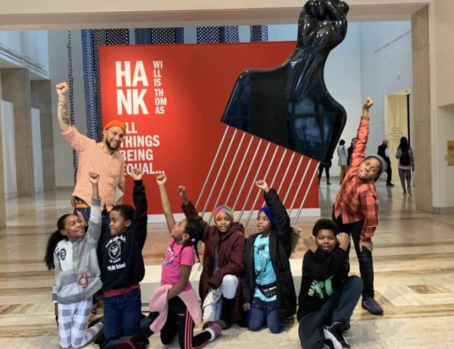 Stevenson and a group of King School students pose with fists raised in front of a sculpture by Hank Willis Thomas at the Portland Art Museum.