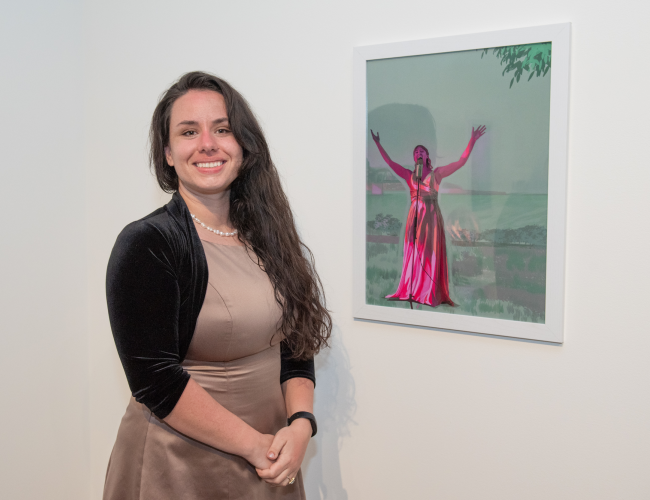 Shelbie Loomis standing next to her artwork on a gallery wall.