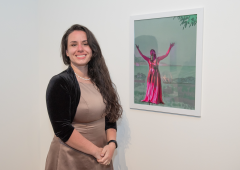 Shelbie Loomis standing next to her artwork on a gallery wall.