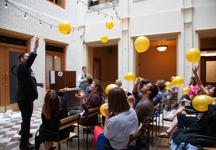 An audience at a social practice event play with yellow balloons