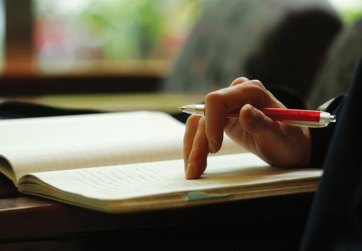 hand resting on a note pad holding a red pen, ready to take notes