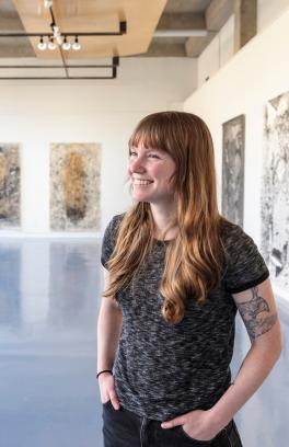 Graduate student standing in gallery with her graduate project exhibition in background