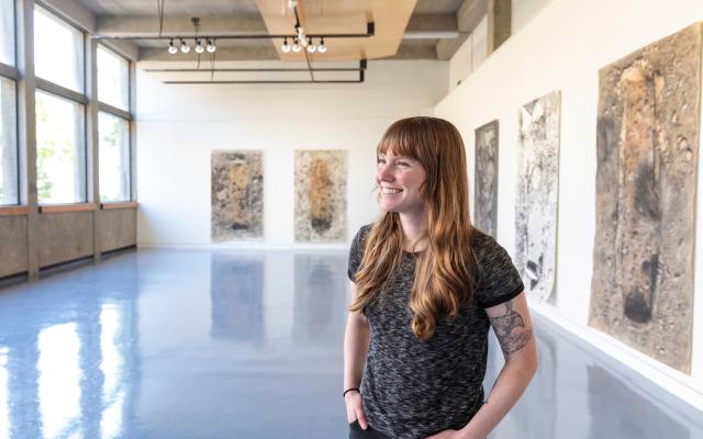 Graduate student standing in gallery with her graduate project exhibition in background