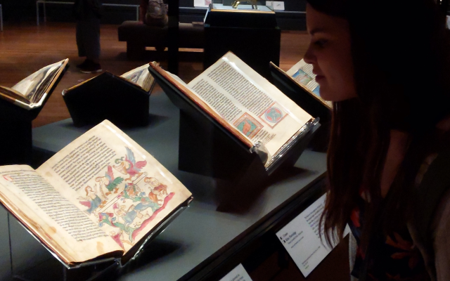 Woman at a museum looking at illuminated manuscripts on display.
