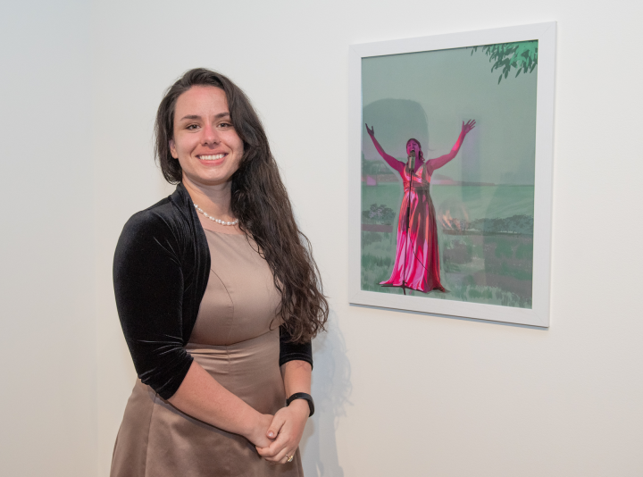 Shelbie Loomis standing next to her artwork on a gallery wall.