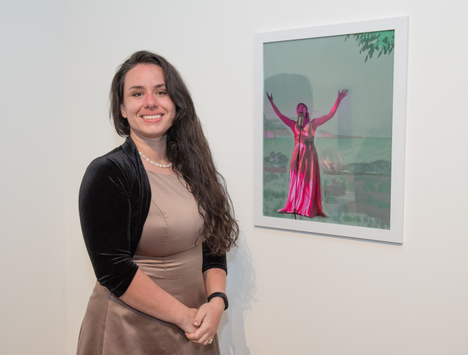 Shelbie Loomis standing next to her artwork on a gallery wall.