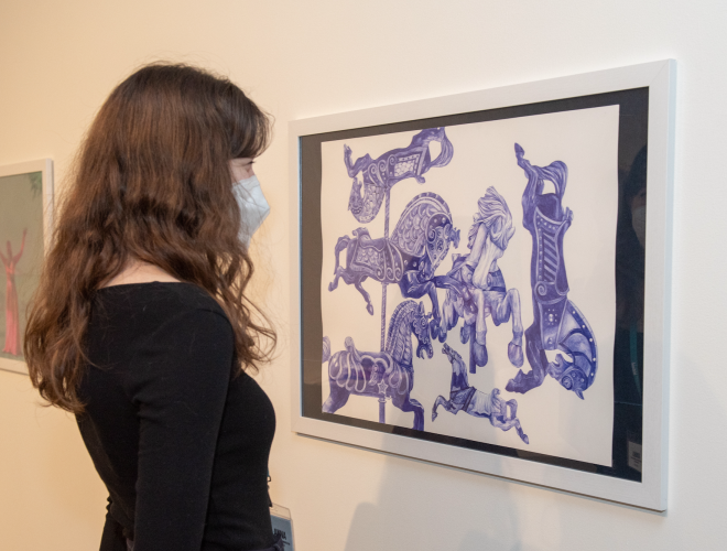 Woman in gallery viewing blue ball point pen drawing of carousel horses.