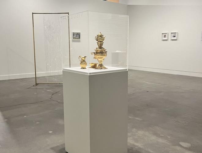 Installation view of gallery with vitrine containing golden tea service in foreground.