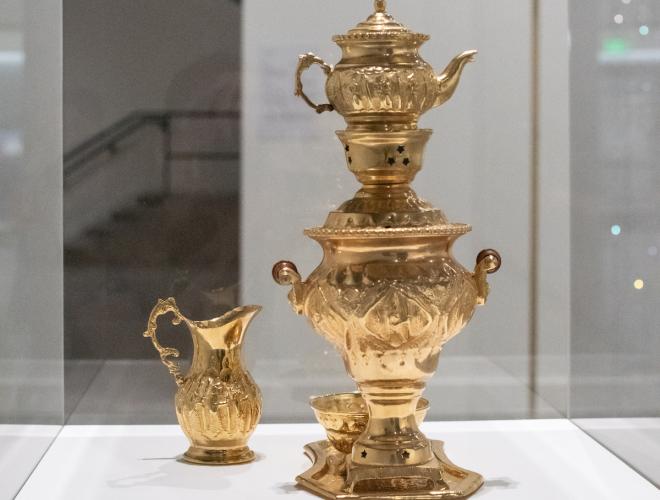 Golden middle eastern style coffee pot displayed in a vitrine.
