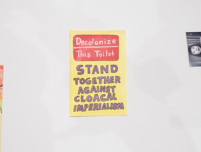 Small drawing that says "Decolonize the toilet" in red and "Stand together against cloacal imperialism" in purple on a yellow background.