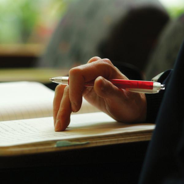 hand resting on a note pad holding a red pen, ready to take notes