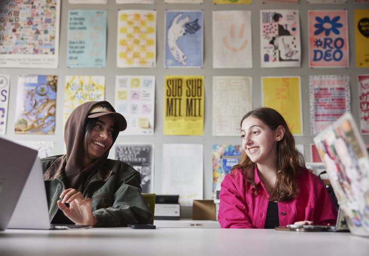 Graphic Design students laughing together while sitting at a studio table