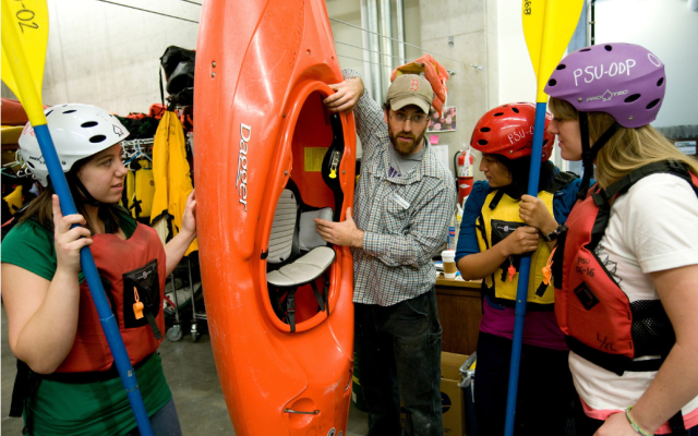 Image of instructor showing three students safety features of a Kayak rental