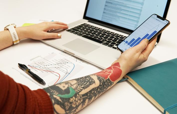 Person holding phone in front of computer, both displaying graphics