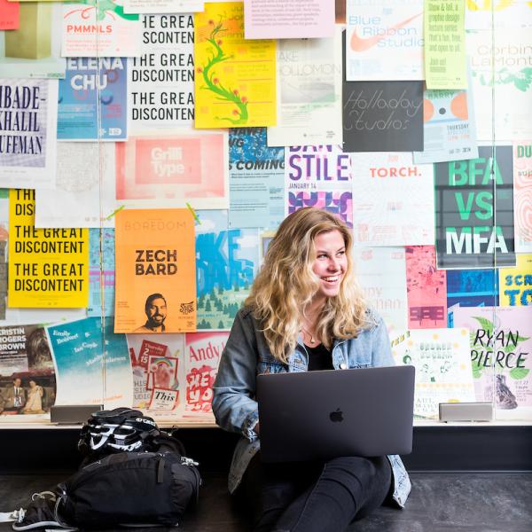 Student working on their computer in front of bulletin board full of posters