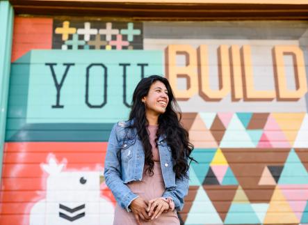 Student standing in front a mural that says "You Build"
