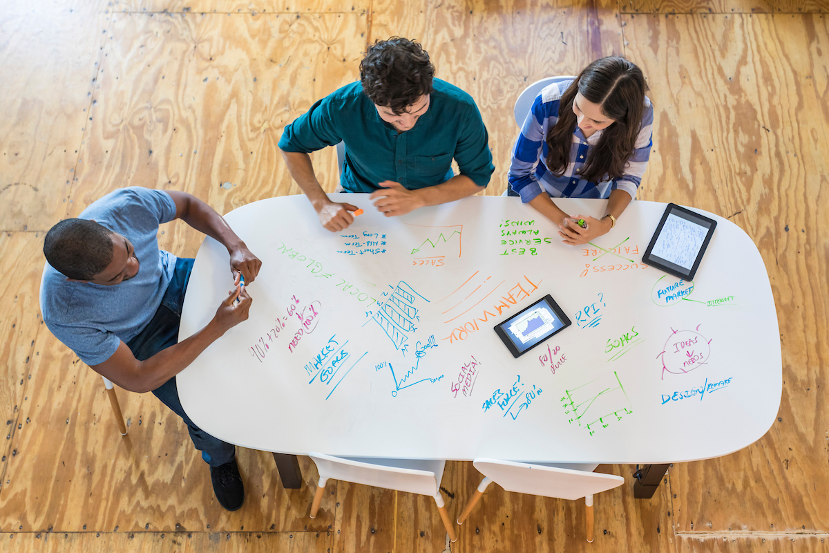 Three students sitting around a whiteboard table