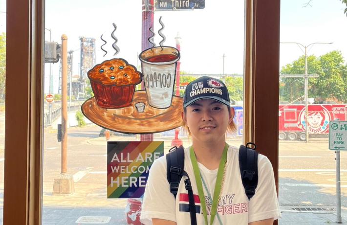 Student next to "All are welcome here" sign