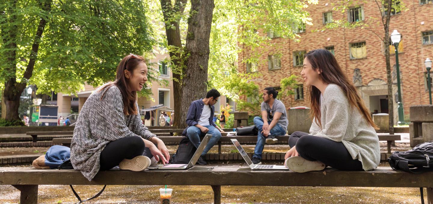 Two students sit facing each other while working on their laptops in the Park Blocks.