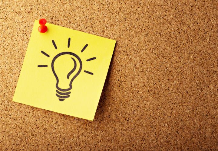 a yellow sticky note with a drawing of a light bulb tacked onto a bulletin board