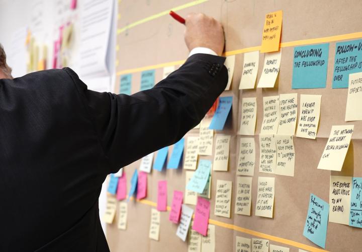 person writing a sticky note to put on a board of organized notes