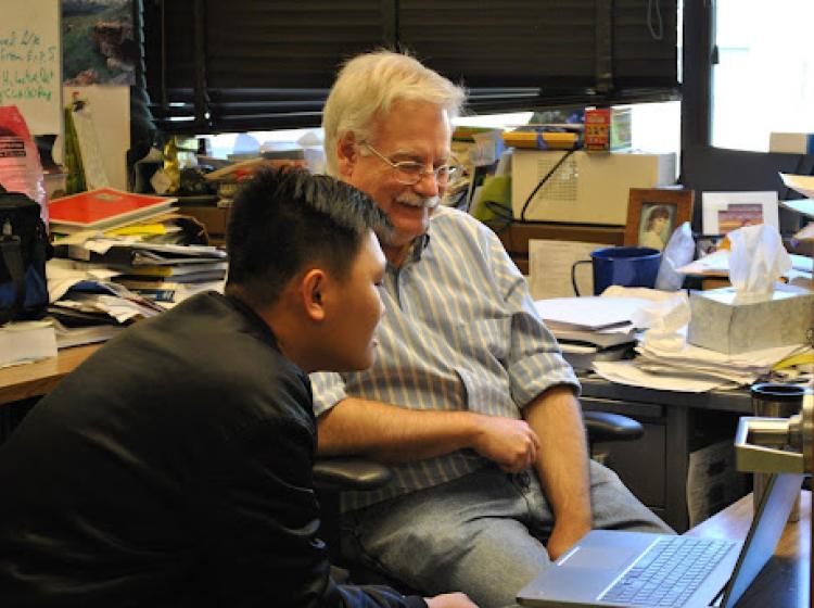 Dr. Dean Atkinson discusses work at his desk with a student. 