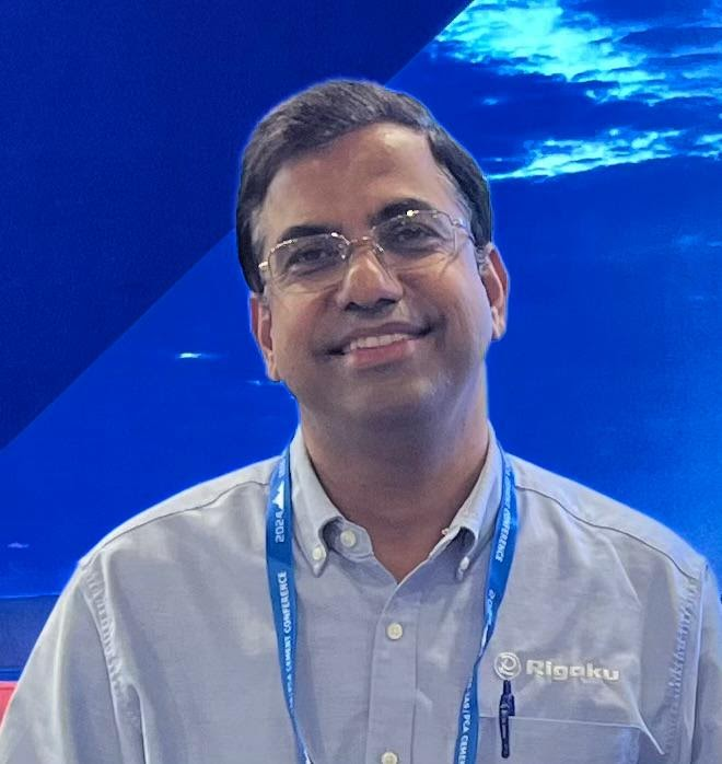 Akhilesh Tripathi, a brown skinned man smiling in front of a watery blue background. 