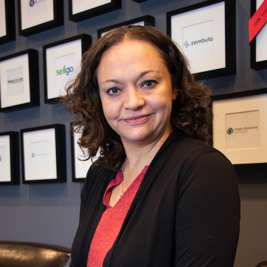 A professional portrait of Andrea Goforth, a light-skinned woman with midlength wavy brown hair, wearing a black coat and red blouse.
