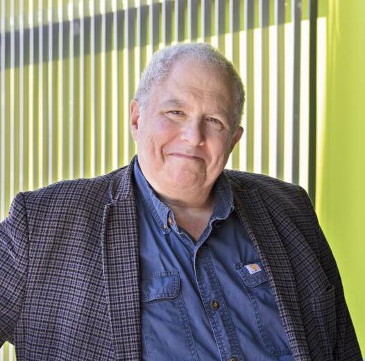 A professional portrait of Rob Strongin, a white man with short white hair, wearing a tartan suit coat over a blue button-down.