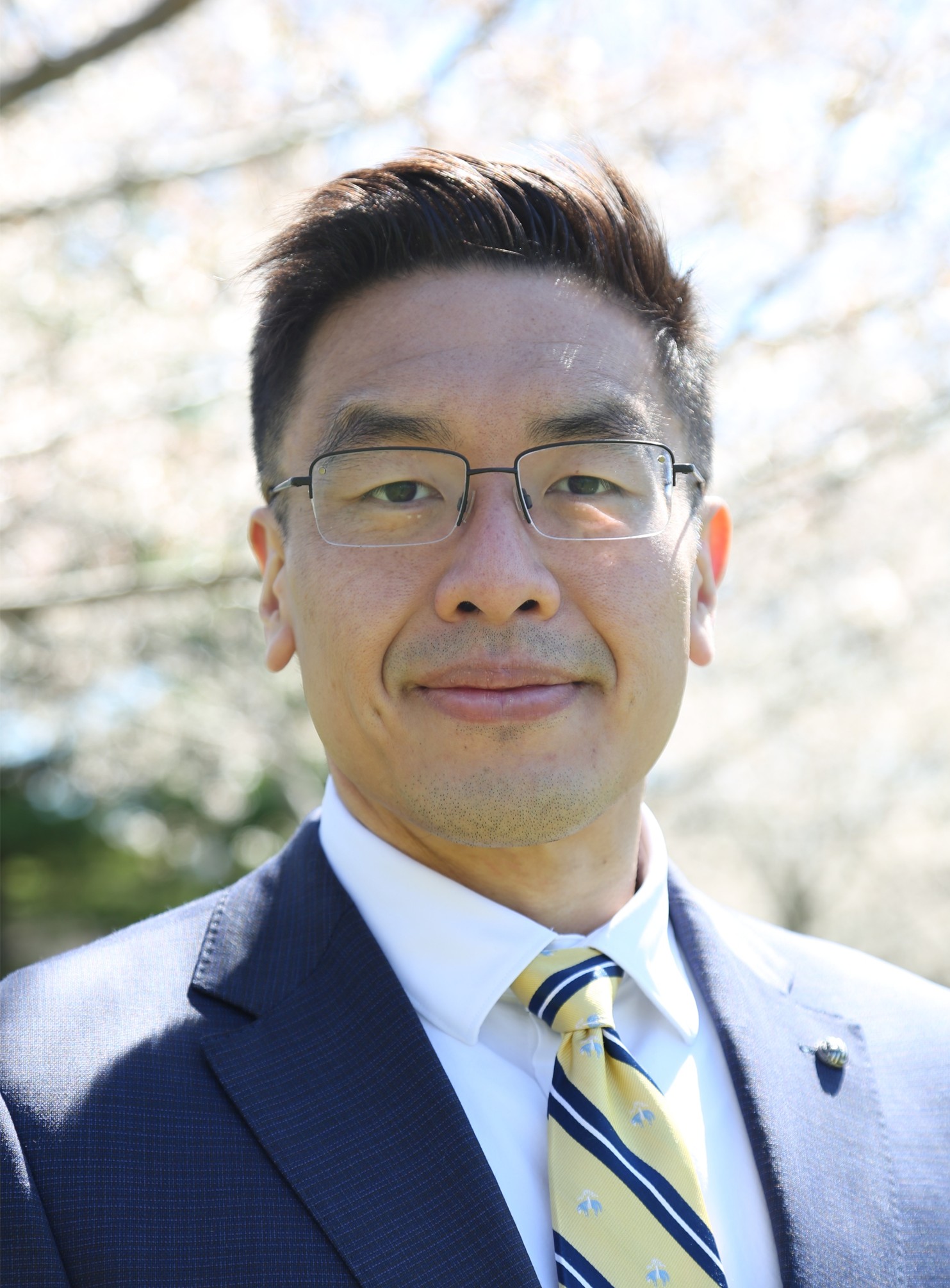 Meng Yang (Matt) Wu, a tan man wearing glasses and a dark blue suit, in a professional portrait outside.