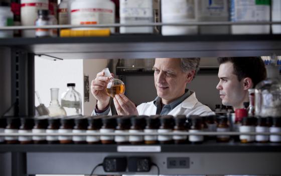 A professor holds glassware filled with orange liquid.