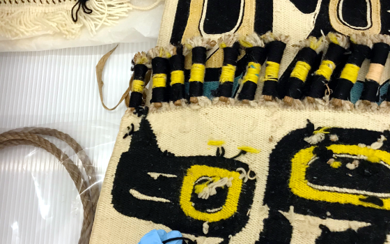 Gloved hand holding fiber on an indigenous weaving laid on a table