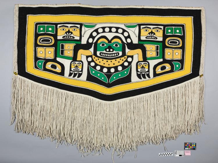 A Chilkat robe, a woven wrap with a long white fringe along the lower edge and featuring images of stylized animals