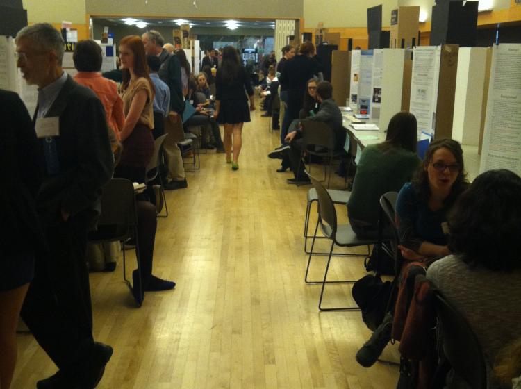 A science fair, a lot of people on either side of a corridor with trifold boards