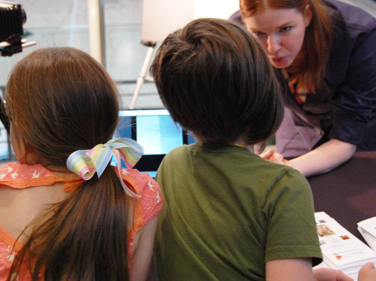 Two children in foreground facing away towards a woman in the upper right of the frame