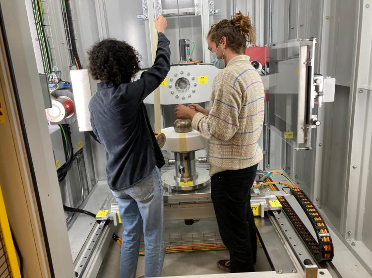 Two people in a large CT scanner standing to either side of a platform