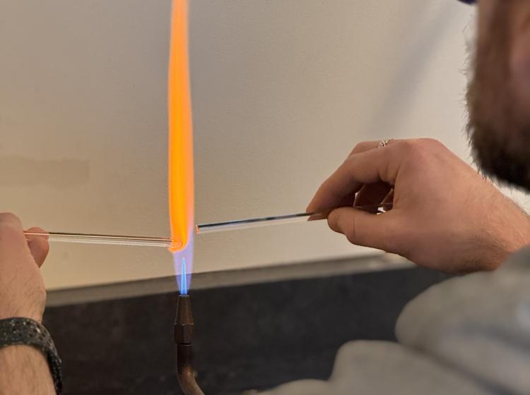 A grad student in glassblowing course using a torch on a glass rod.