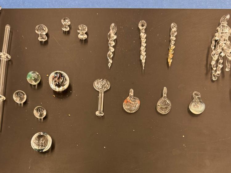 Overhead shot of black tabletop with multiple small pieces of glassware, some are spirals and others are rounded ball shapes. 