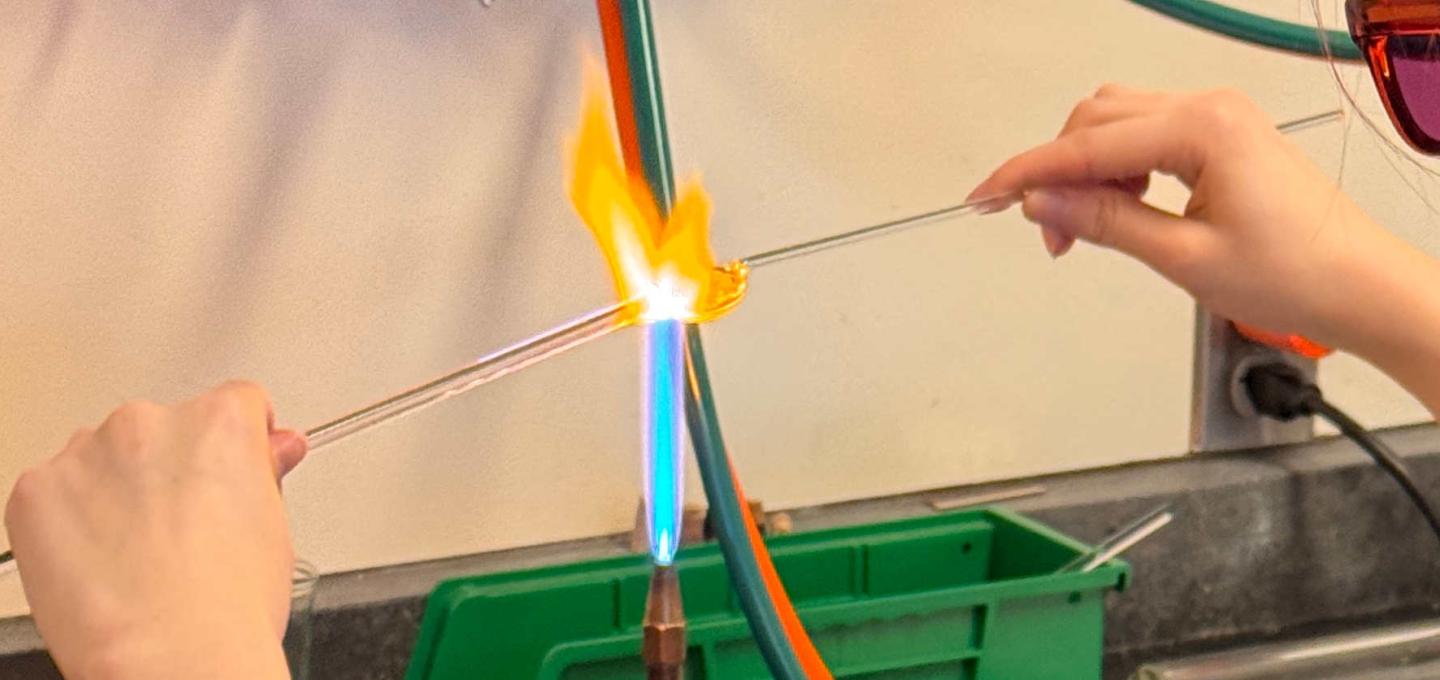 Cropped image of student working a tube of glass over a flame with two hands.