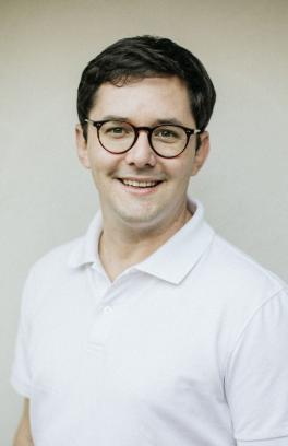 Robert Knowles is smiling for the camera standing in front of a light colored wall wearing a white polo shirt