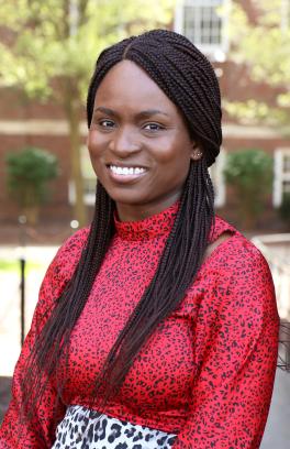 Professional photo of Dr. Tobi Odeleye, a black woman with long black braided hair. She is wearing a red, high-neck blouse with a black dot design. She is seated and smiling with a blurred outdoor background.